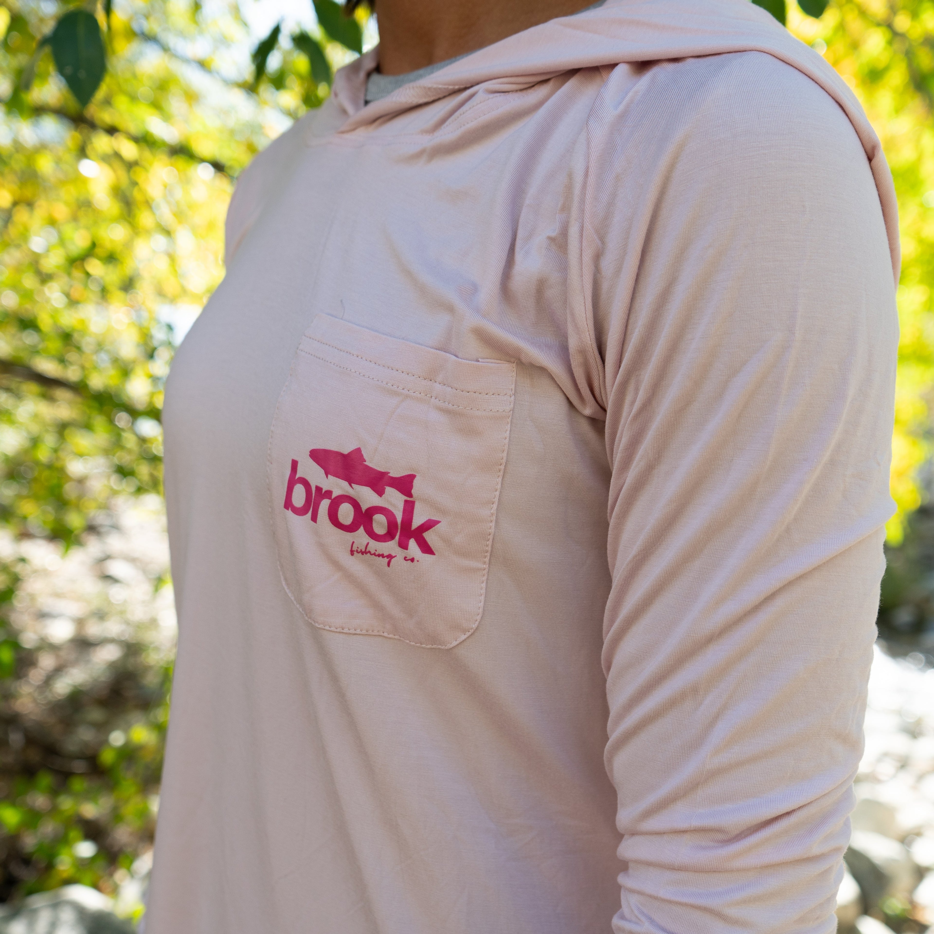 Detailed view of the front pocket and embroidered Brook Fishing Co. logo on the women’s pink bamboo sun hoodie.