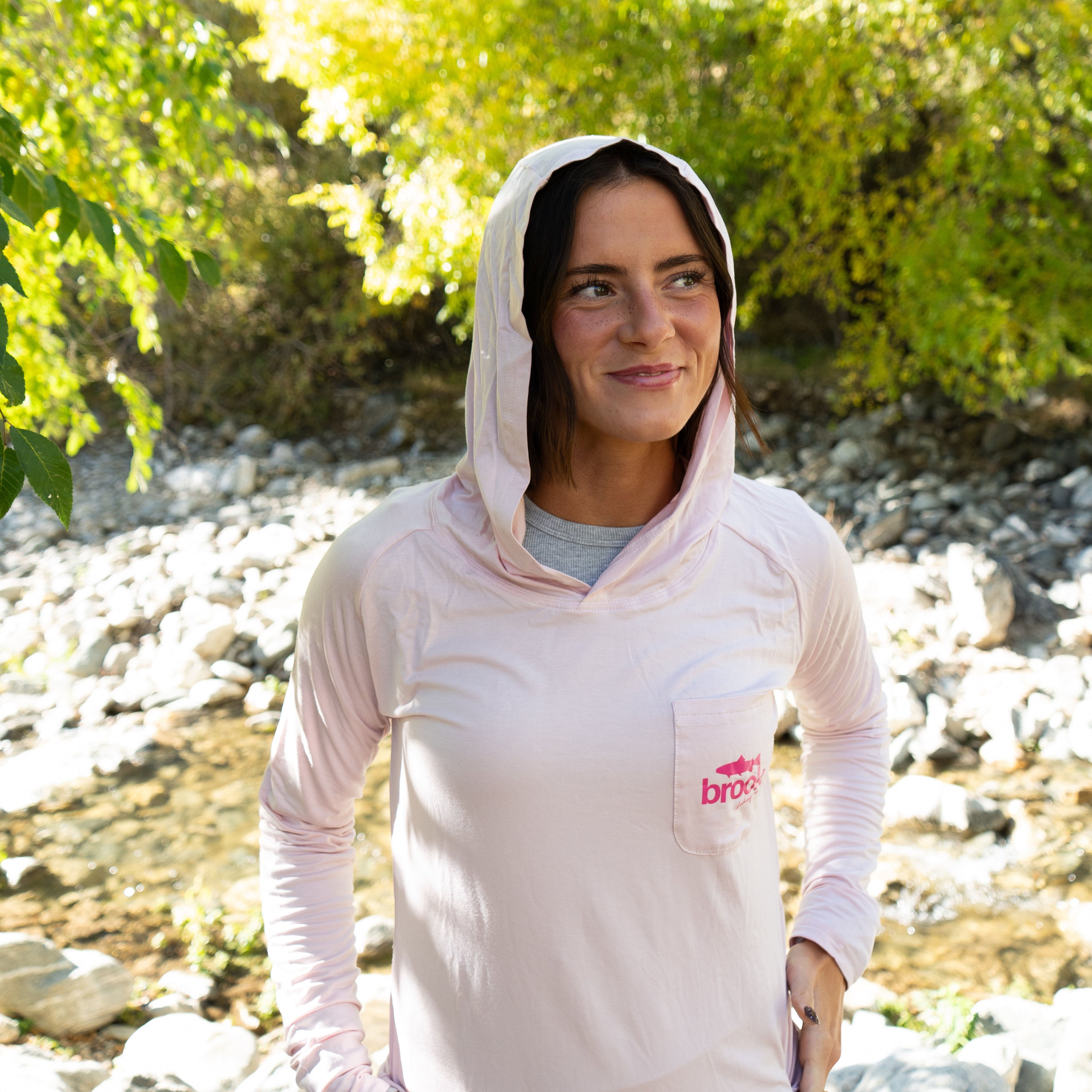 Female angler casting fly line on the river while wearing a light pink bamboo sun hoodie designed for women.