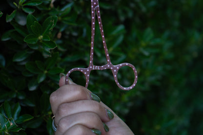 Hand holding a pair of pink scissors against a blurred green background