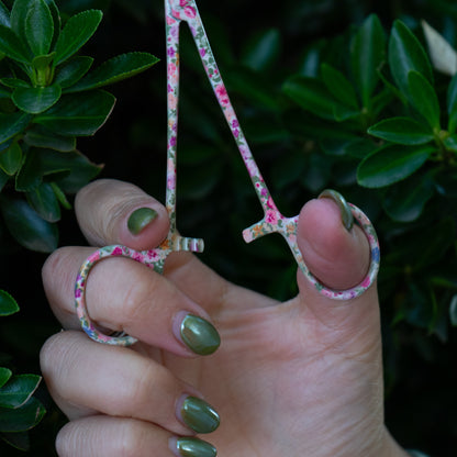 Close-up of a hand opening Brook Floral Hemostats, showing the locking clasp mechanism between the finger holes and the floral stainless steel finish.