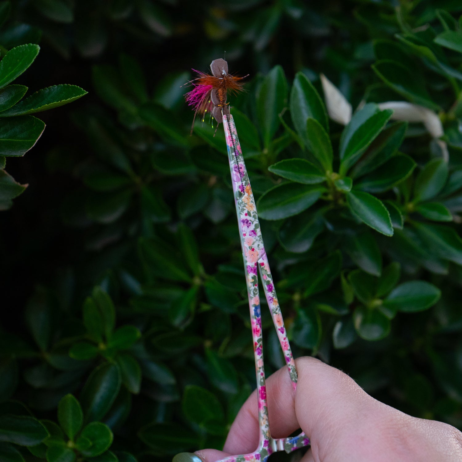 Brook Floral Hemostats holding a dry fly in the tip, showing precise grip and control with feminine floral stainless steel design for women fly fishers.