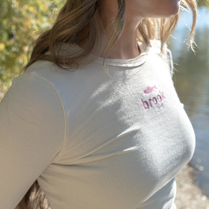 Soft cream modal long sleeve top with curved hem and pink logo on chest.