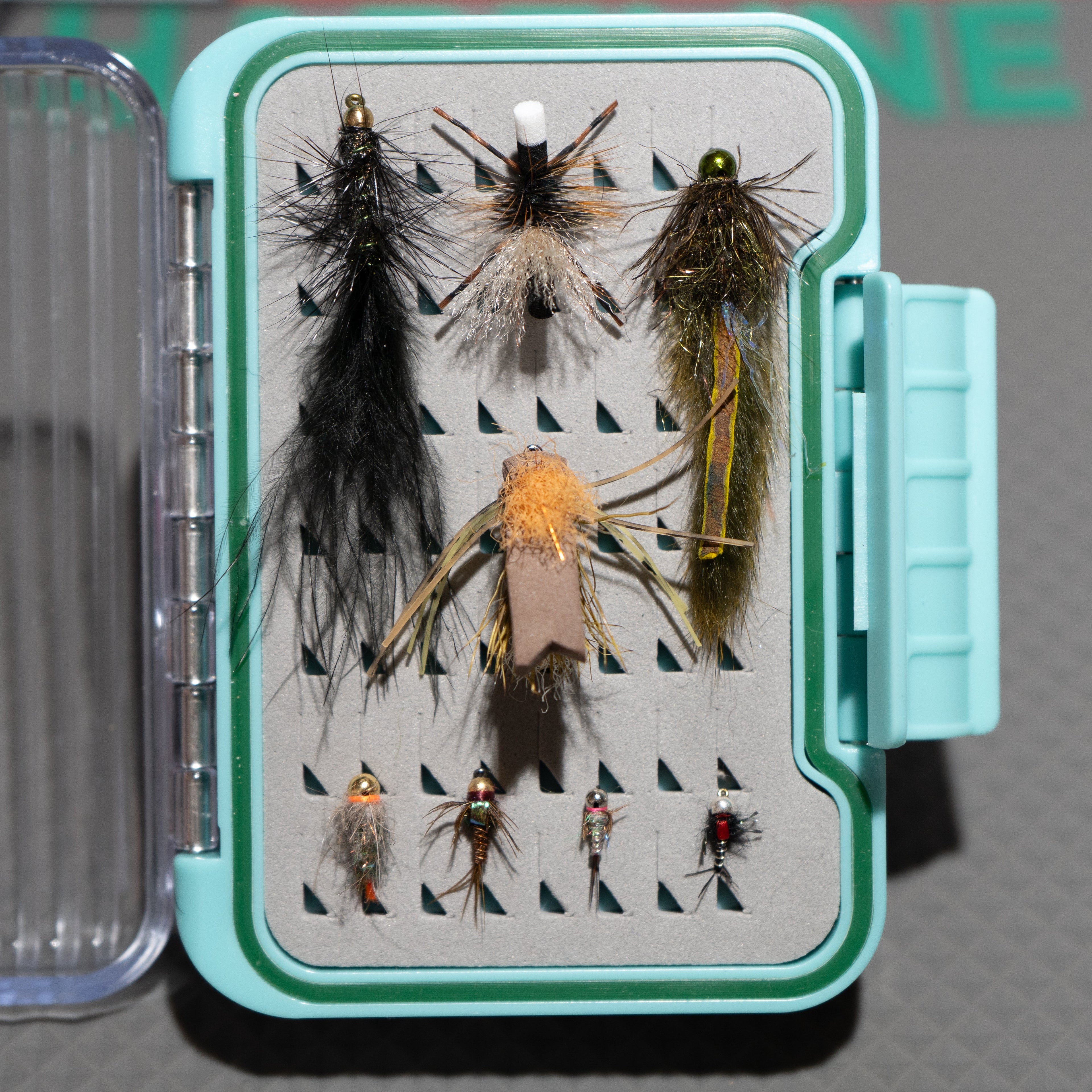 Collection of fly fishing lures in a box on a gray background