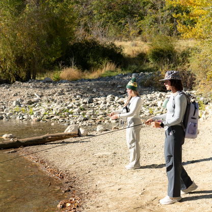 Woman fly fishing by the shoreline wearing the gray Brook Fishing Co. Stillwater Modal Tee, showcasing its soft ribbed fabric and easy movement.