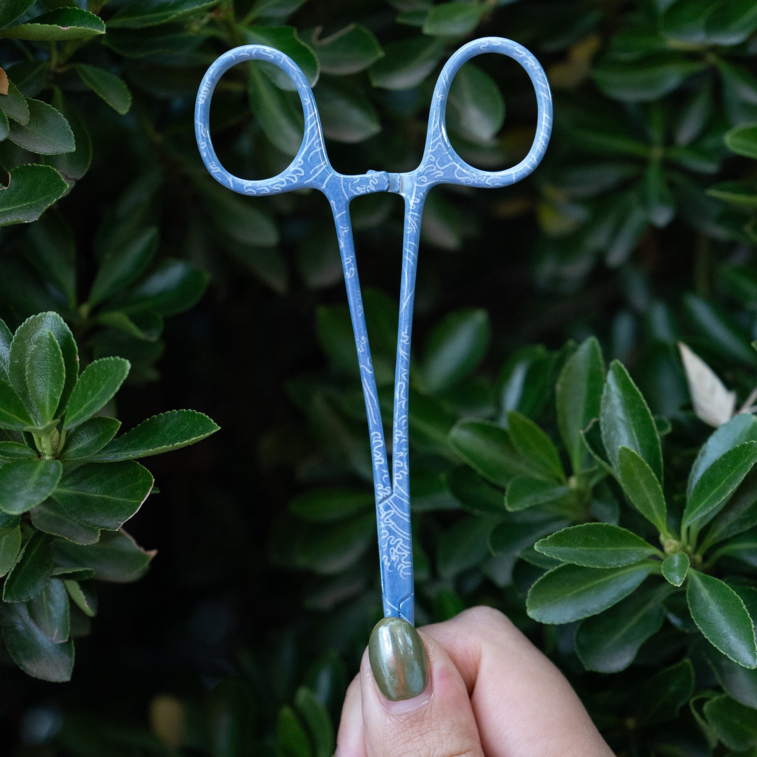 Hand holding Mini Waves fishing hemostats closed, showing locking mechanism and wave pattern handle.