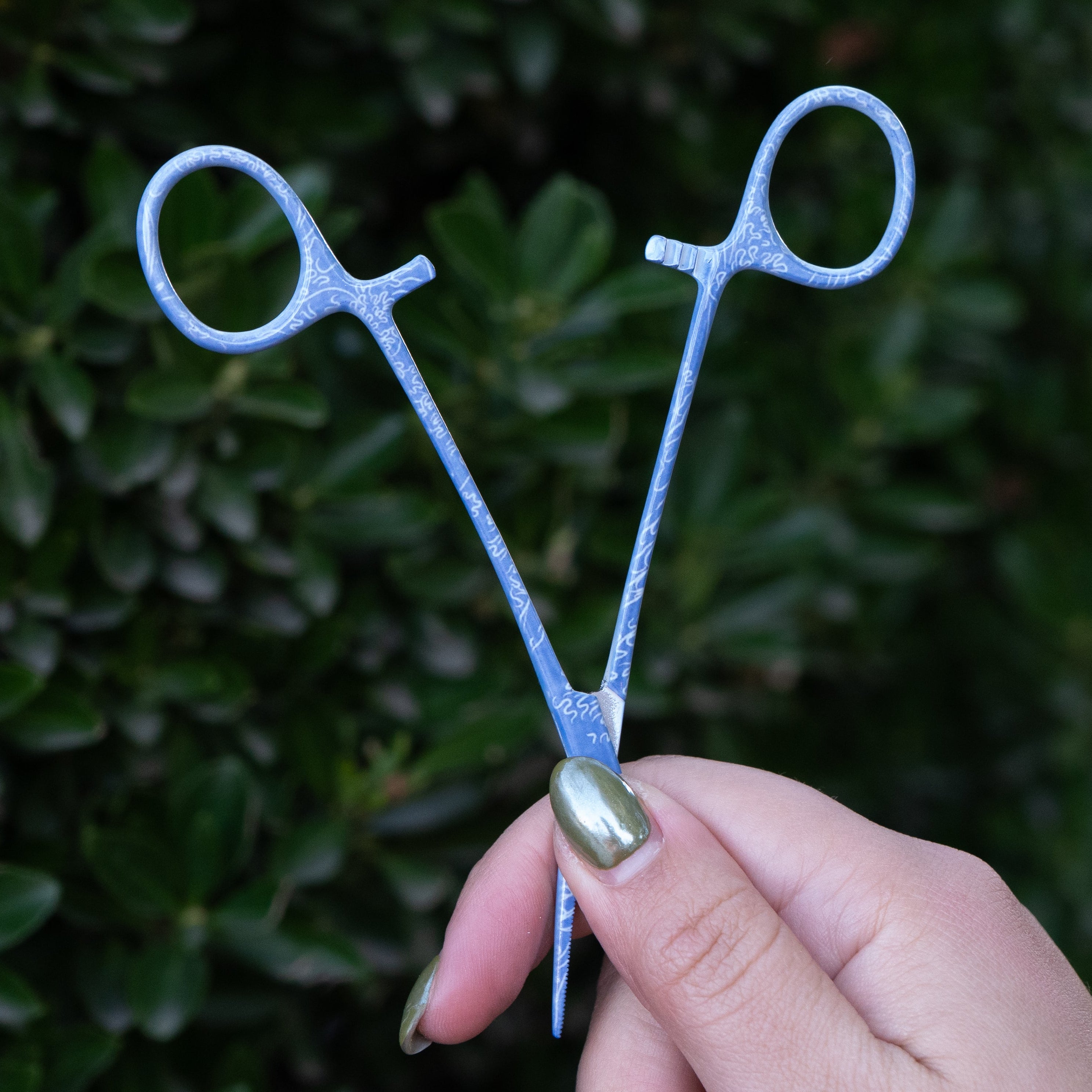 Hand holding Brook Fishing Co. Mini Waves stainless steel fishing hemostats open to show width and grip design.